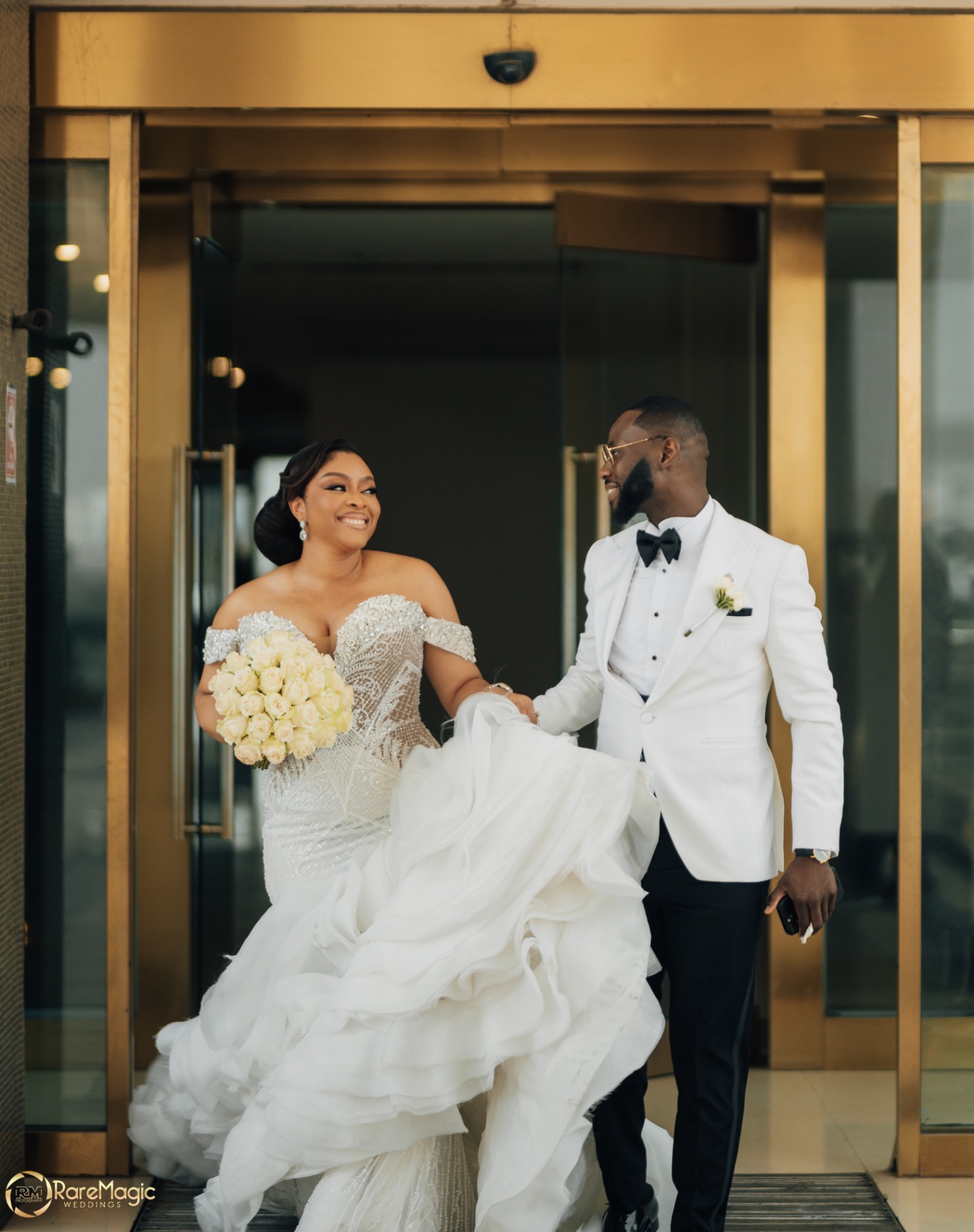 Bride and groom laughing together as they step through gold-framed glass doors