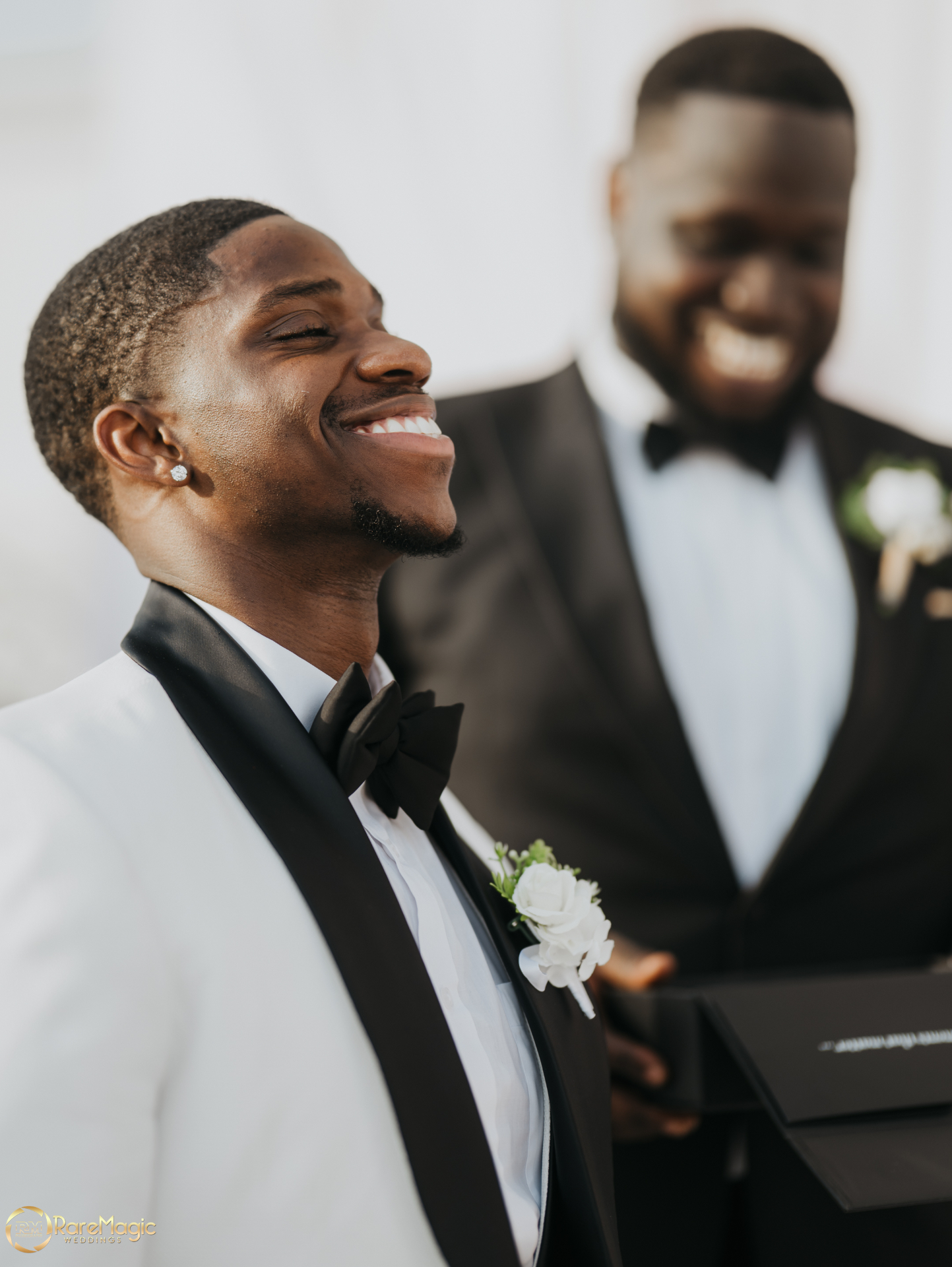 Groom smiling during the ceremony with a groomsman blurred in the background