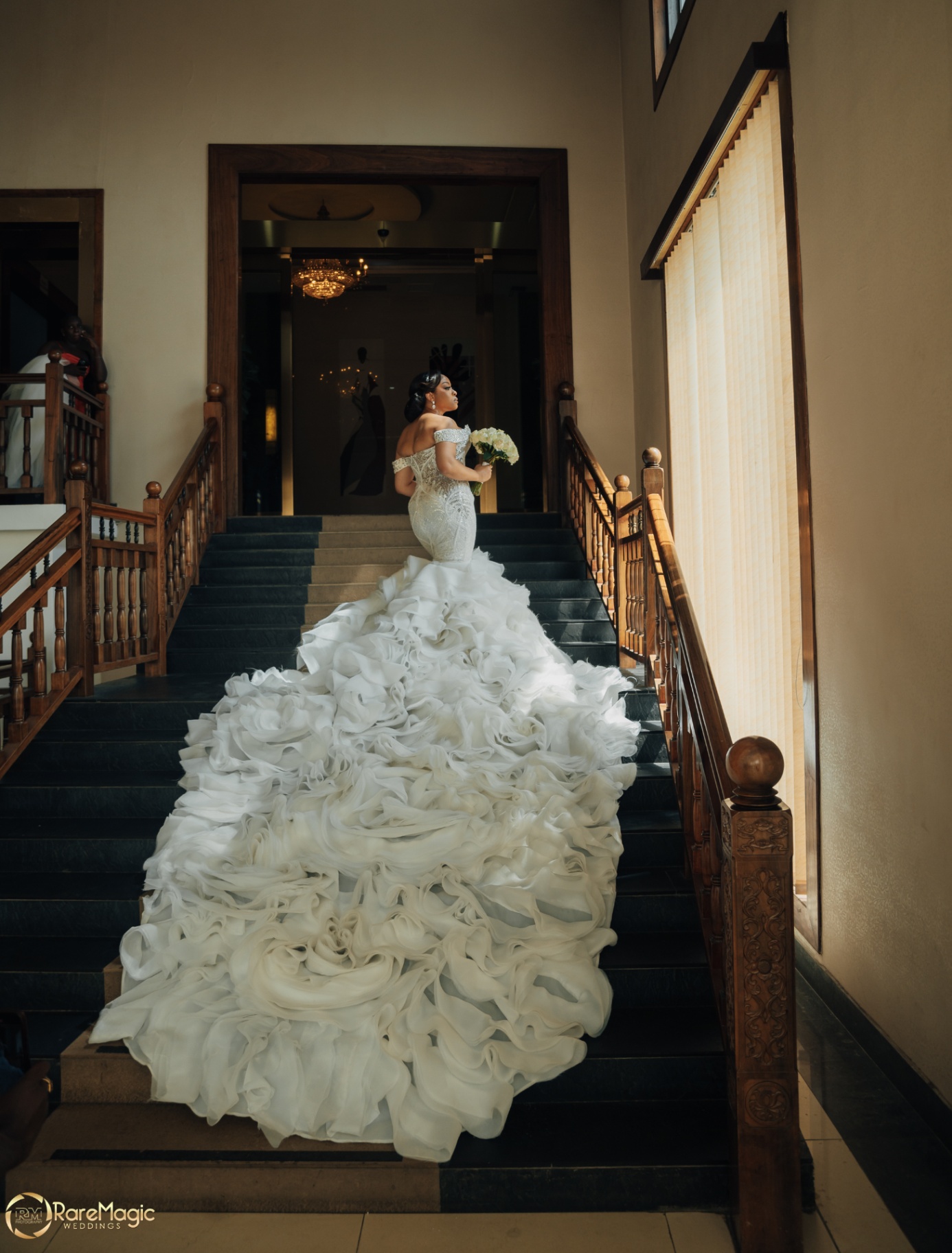Bride on a grand wooden staircase with a voluminous ruffled gown train cascading down the steps