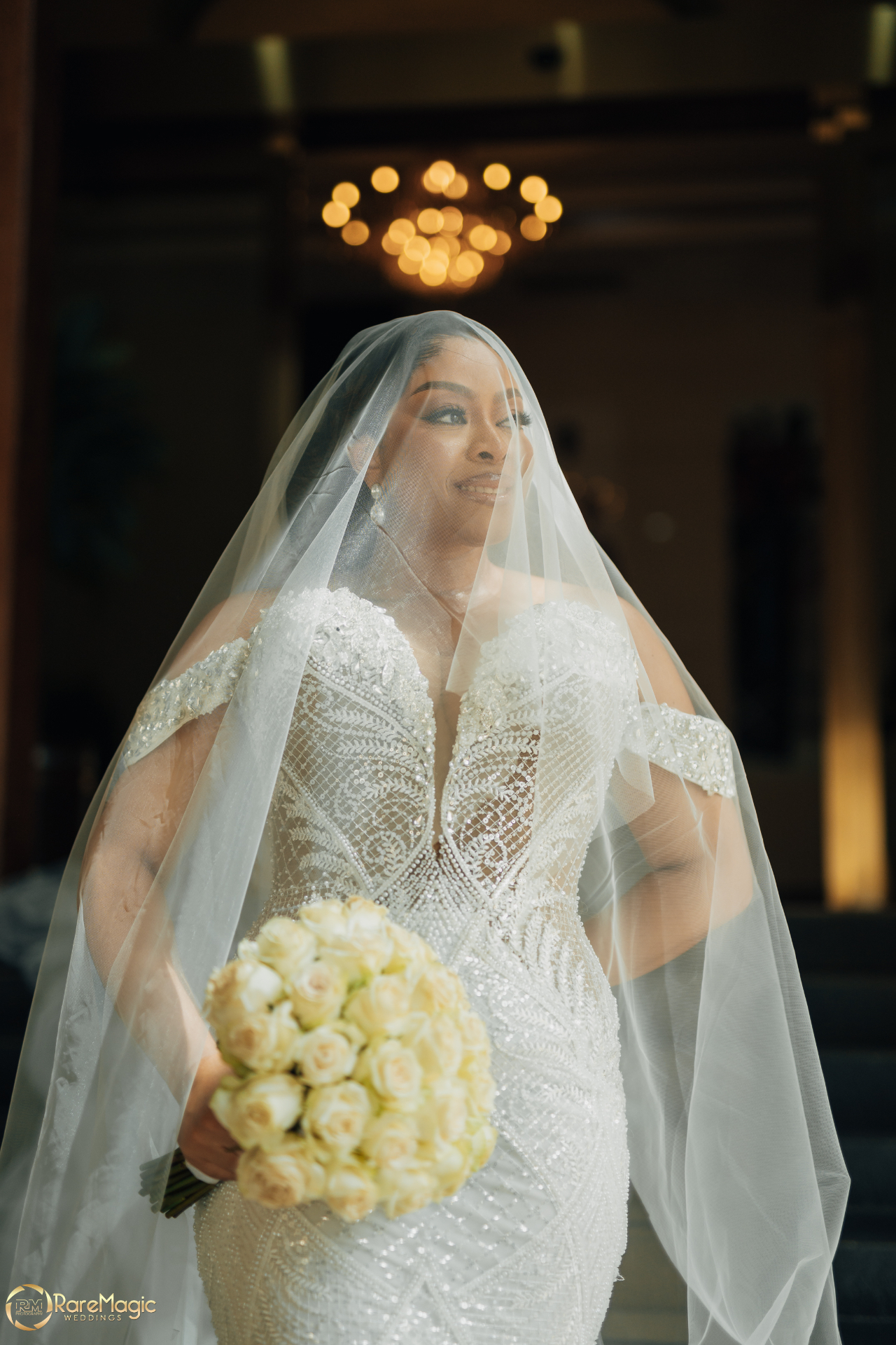 Bride beneath a cathedral veil holding a cream rose bouquet under a warm chandelier