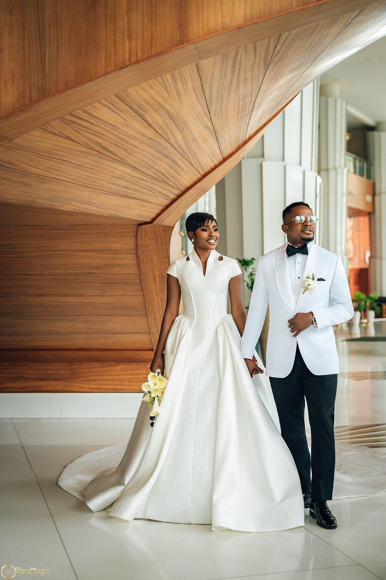 Bride and groom walking hand in hand beneath a dramatic wooden architectural feature