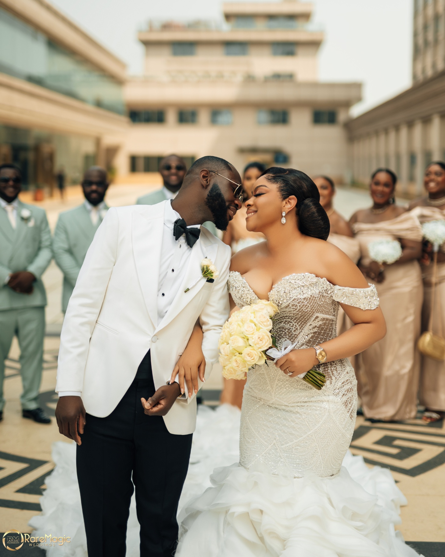 Couple sharing a forehead touch with the full bridal party blurred behind them