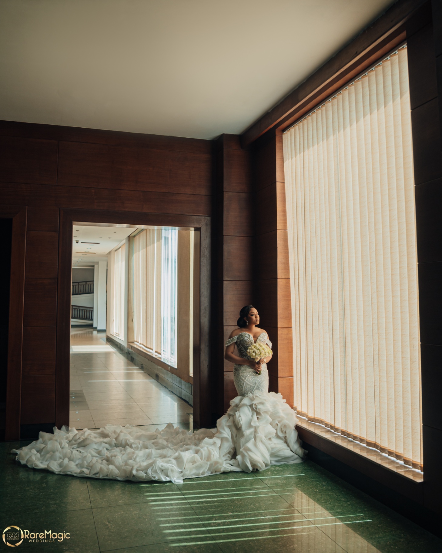 Bride by the window in a sculptural ruffled mermaid gown holding her bouquet