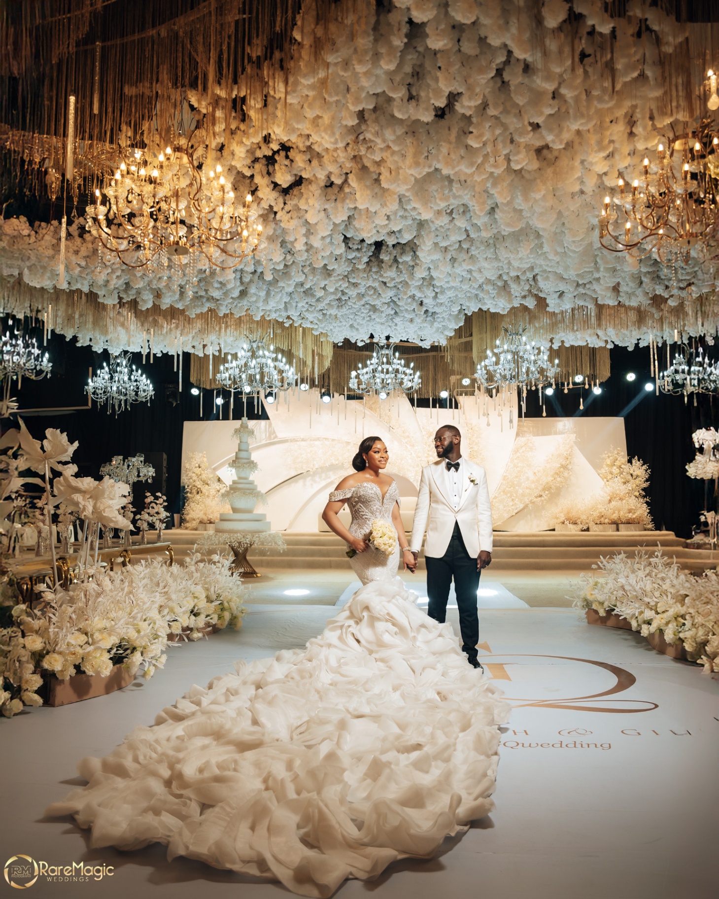 Bride and groom hand in hand on the reception floor beneath a sprawling floral ceiling and chandeliers