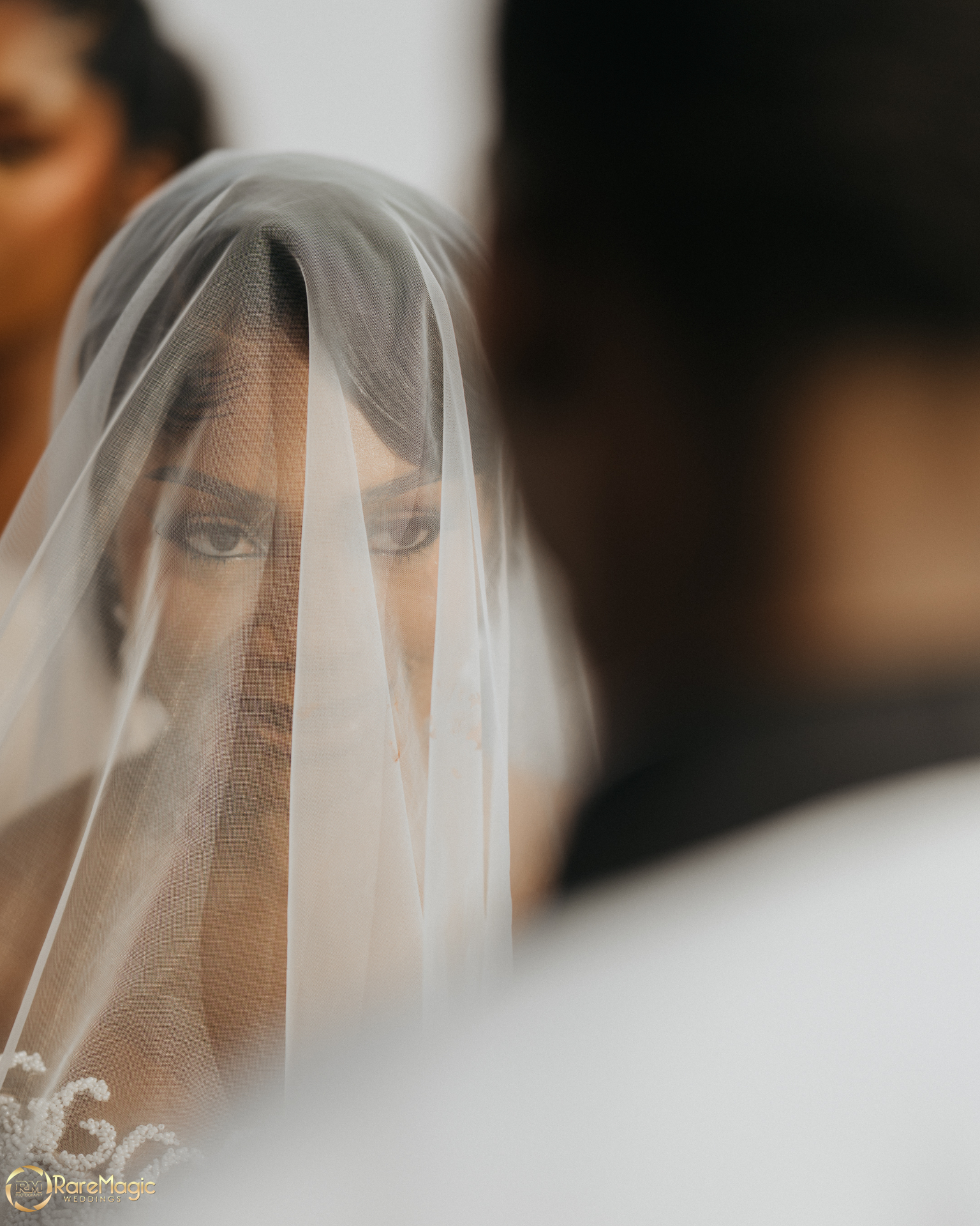 Bride veiled, framed between figures in soft focus
