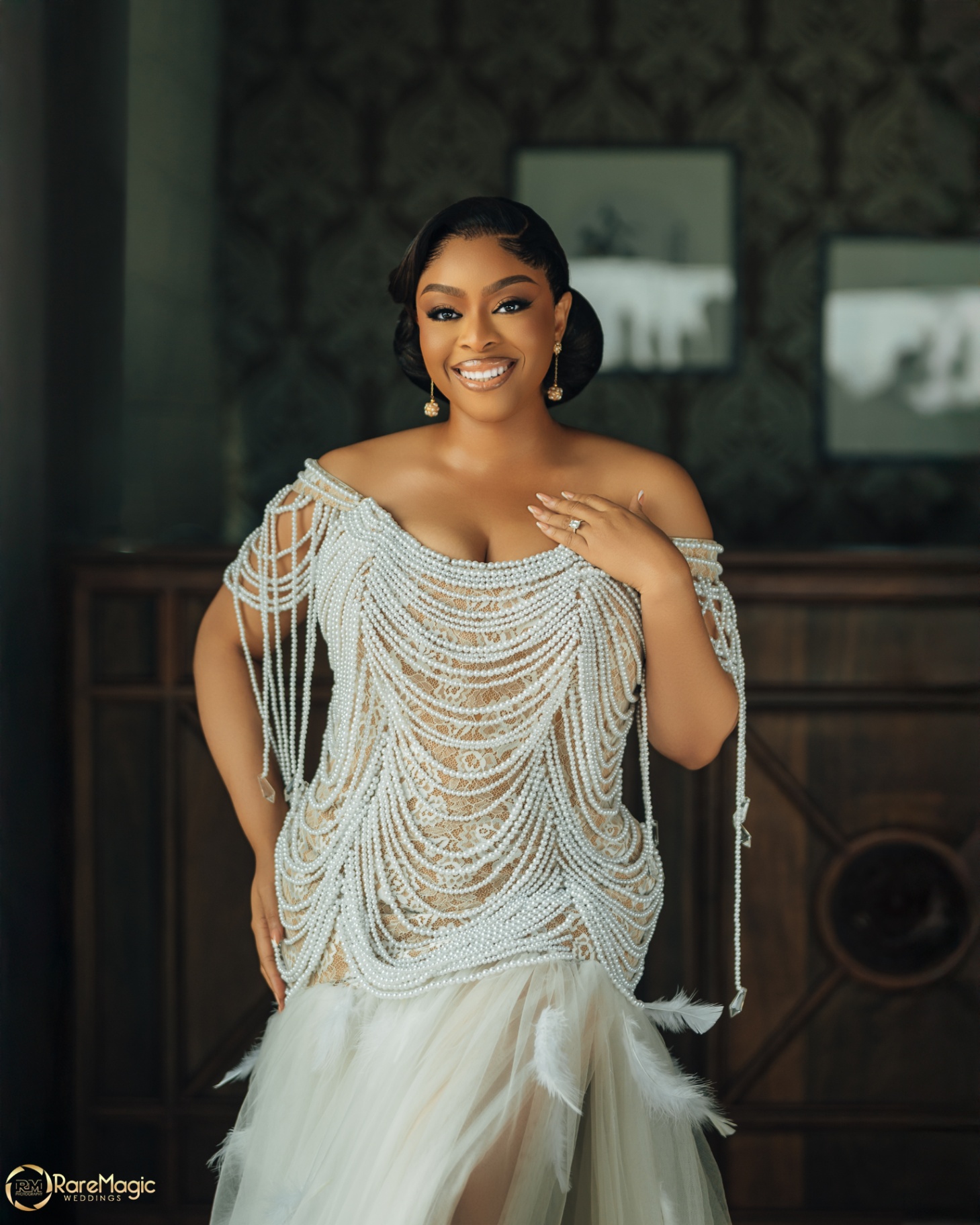 Bride smiling in a pearl-draped lace gown with feather hem