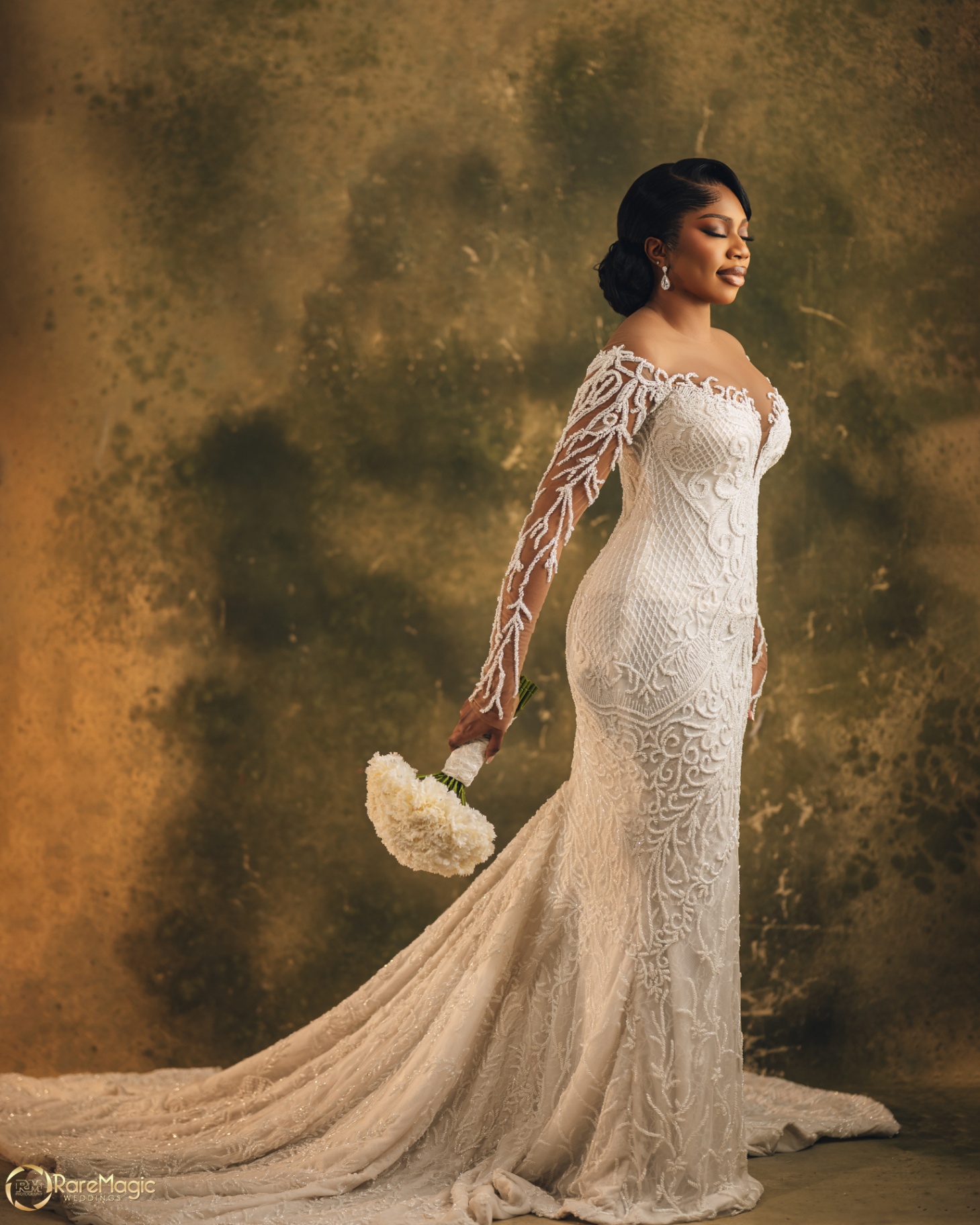 Bride in beaded mermaid gown holding her bouquet against a warm textured backdrop