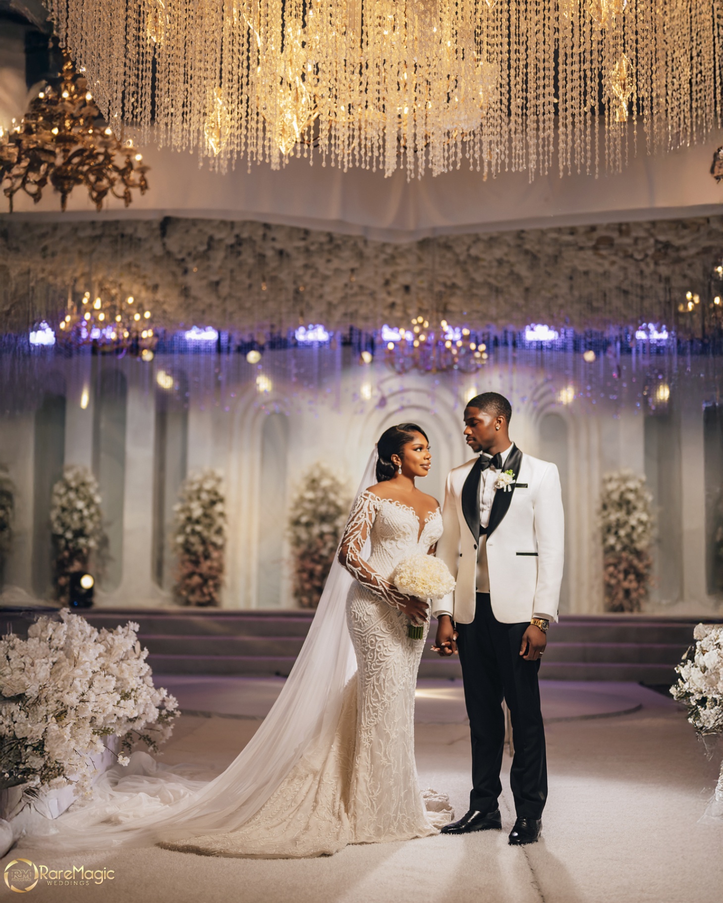 Couple holding hands beneath crystal chandeliers in the reception space