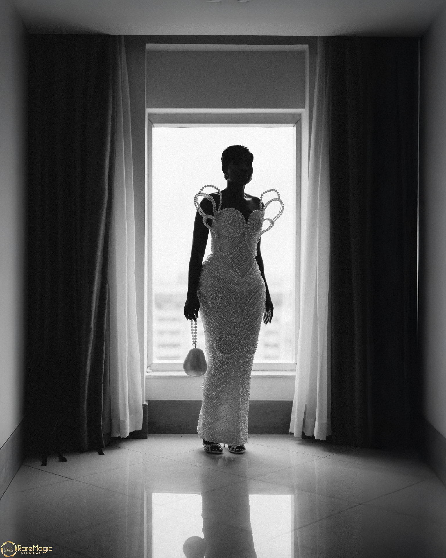 Black and white silhouette of the bride in a sculptural gown by the window