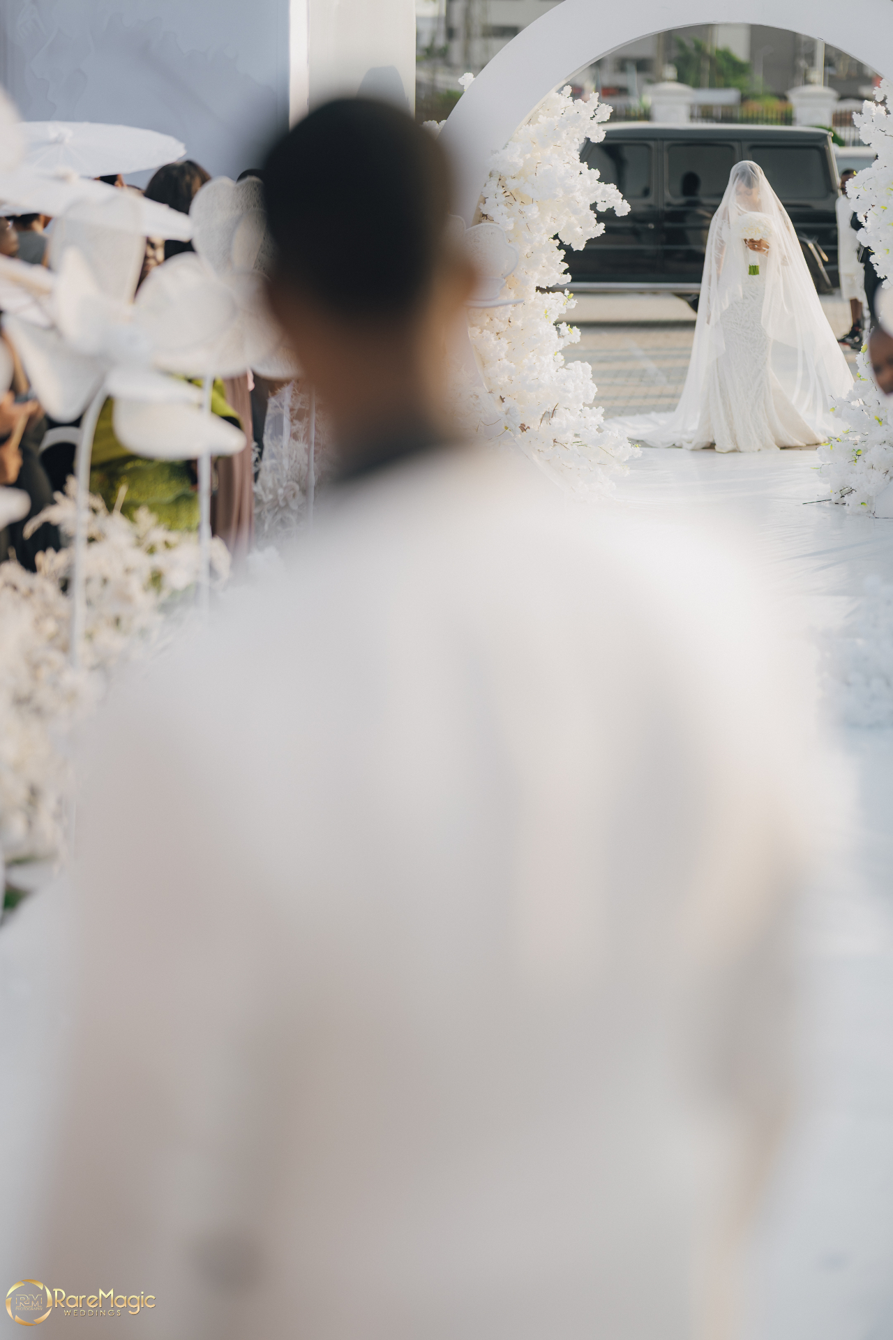 Groom watching the veiled bride arrive through a floral arch