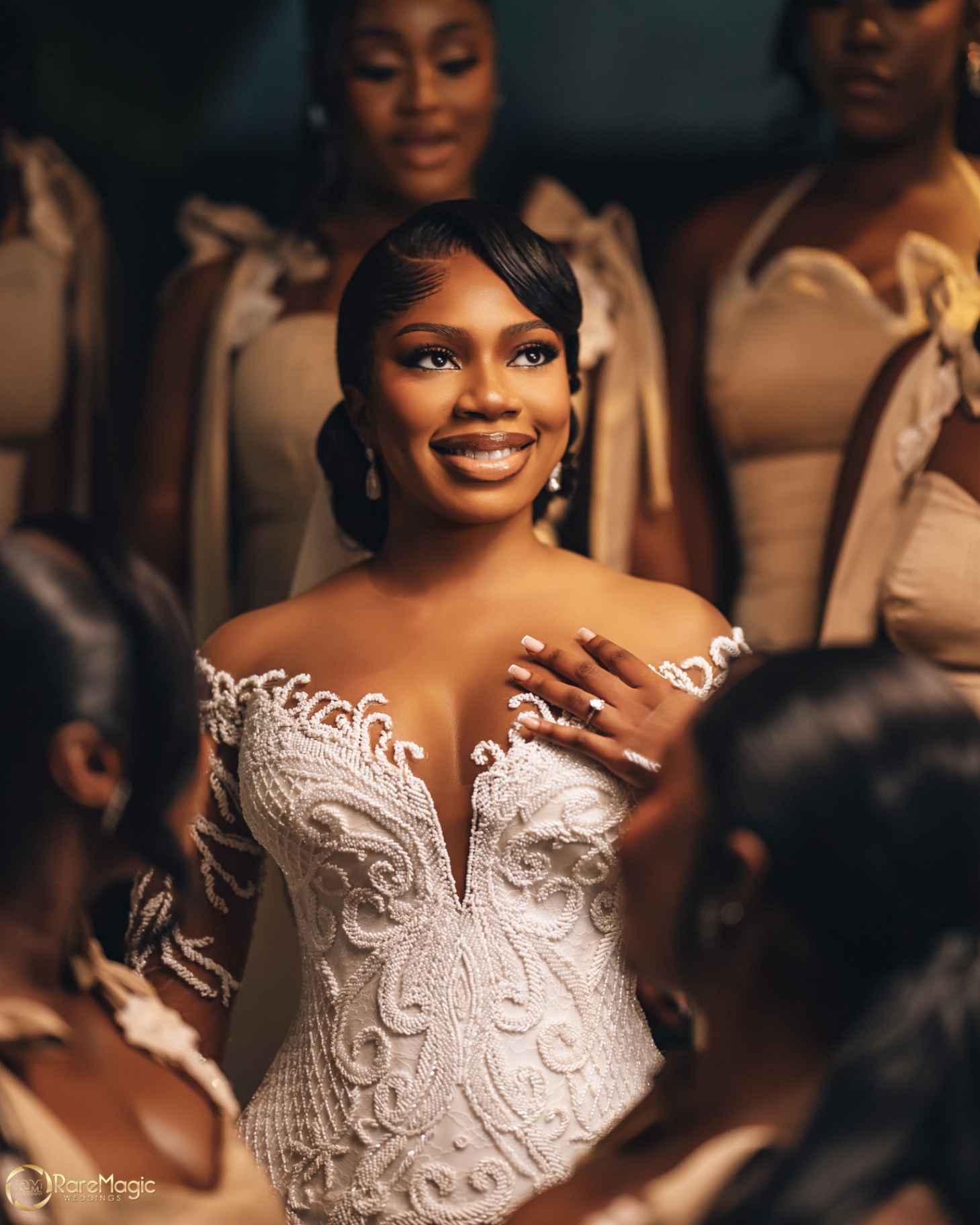 Bride smiling among her bridesmaids with hand on her chest