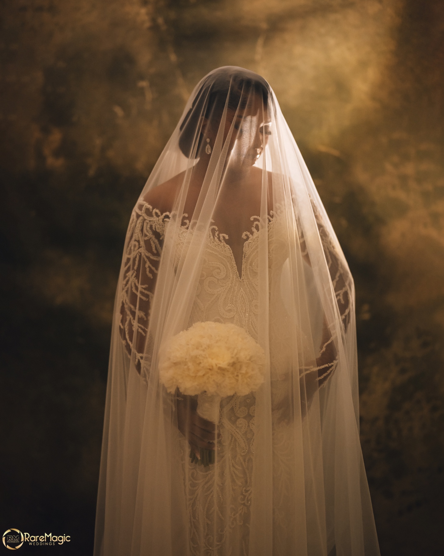 Bride beneath a long cathedral veil holding a white bouquet
