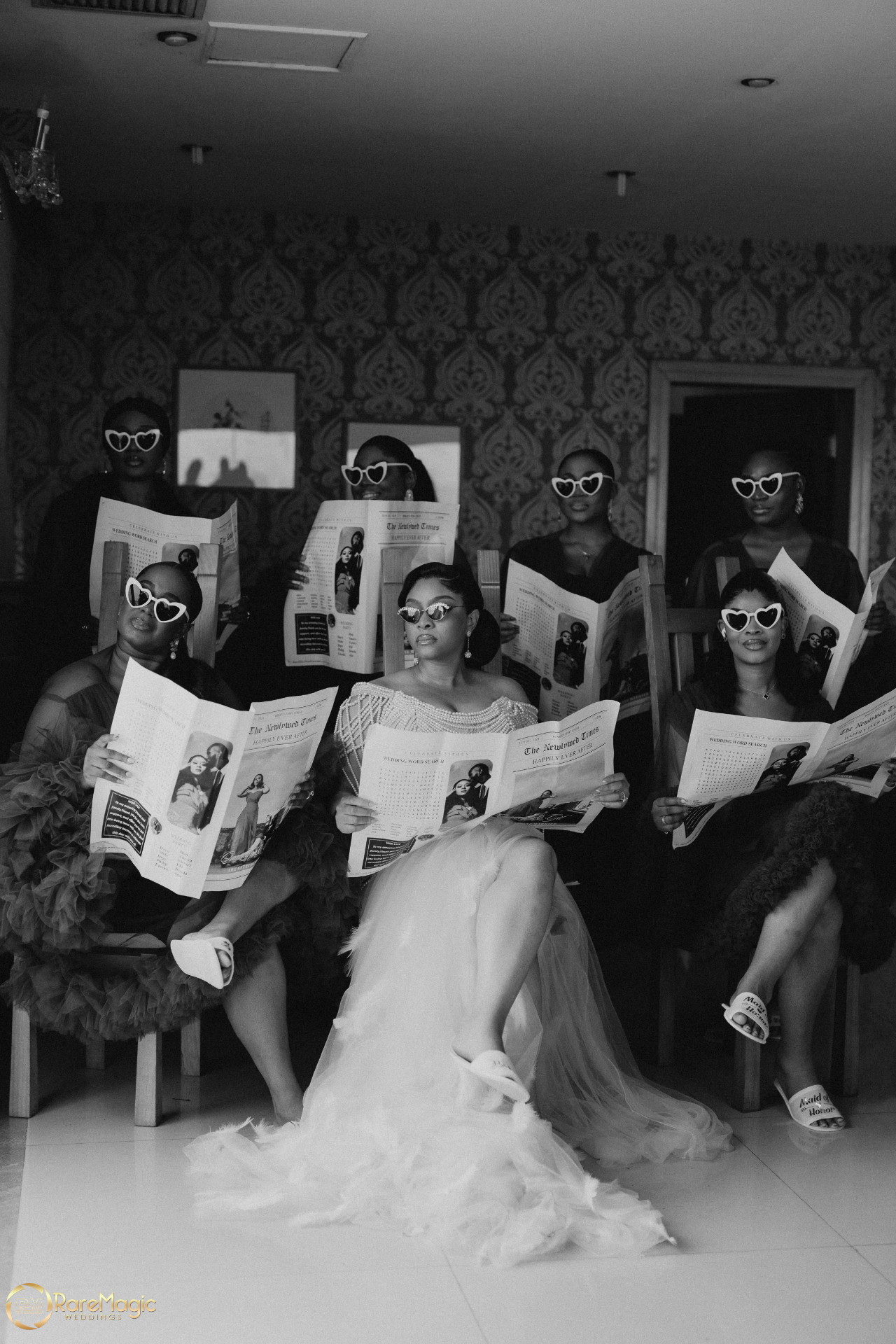 Black and white portrait of the bride and bridesmaids reading wedding newspapers