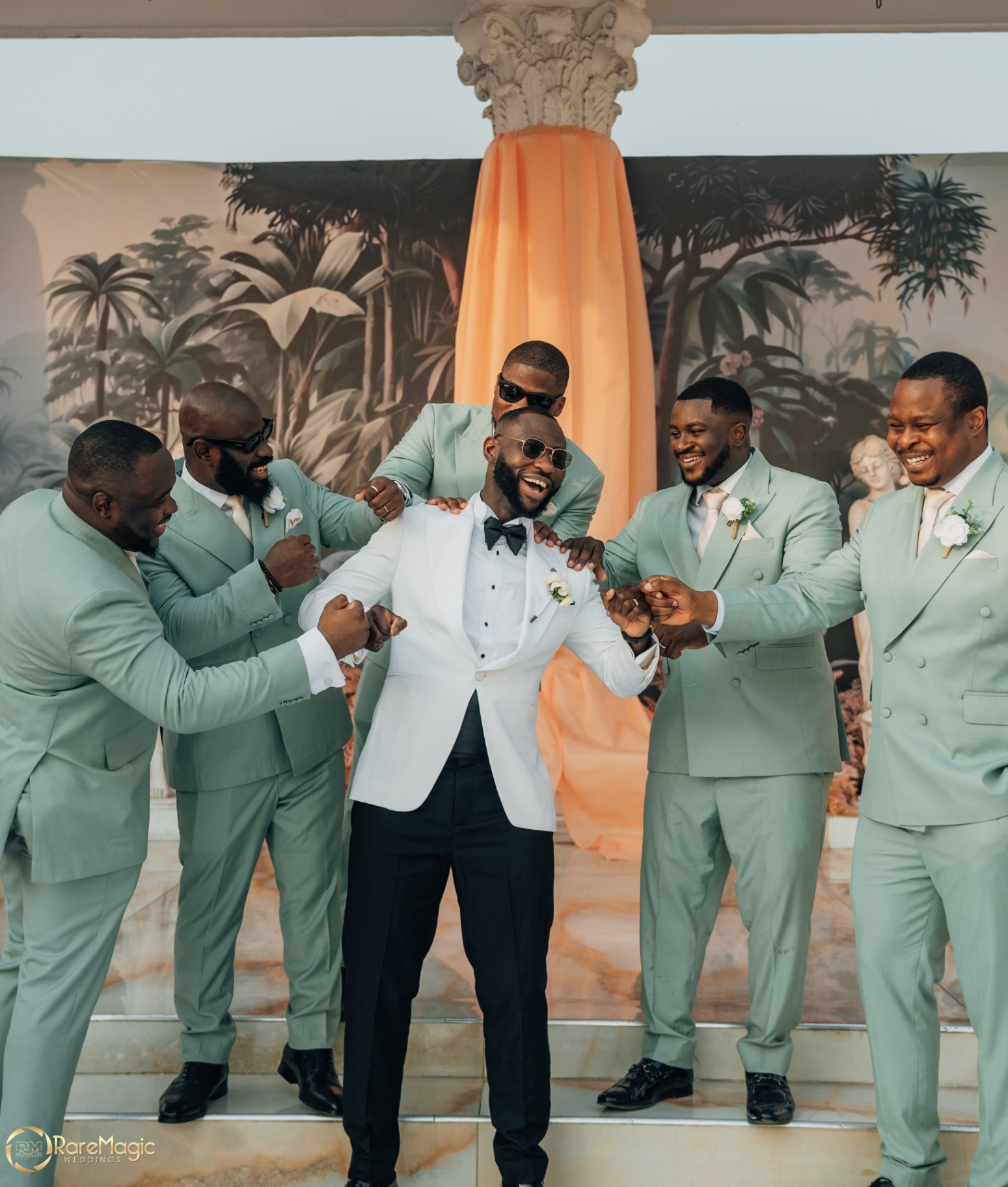 Groom laughing with his groomsmen in sage suits on the pavilion steps