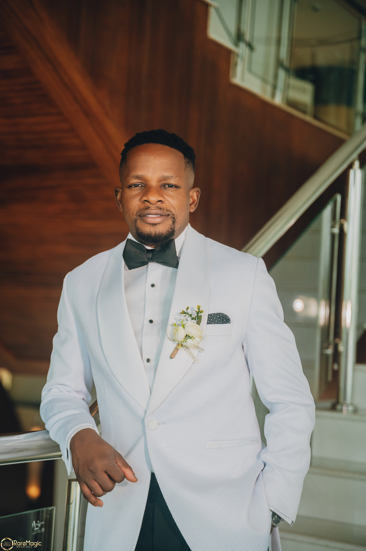 Groom portrait in a white tuxedo leaning against the stair rail